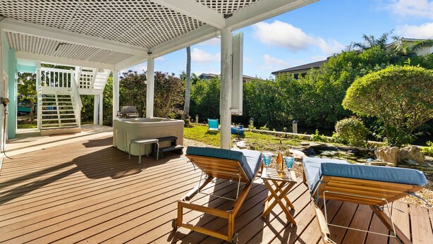 A covered outdoor deck with lounge chairs, a hot tub, and a view of a garden and buildings. - Green Turtle Boathouse/HOT TUB view of the canal (Naples)