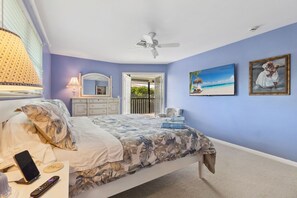 Une chambre à coucher avec un lit, un ventilateur de plafond, une télévision, une commode et un tableau.