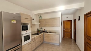 A compact kitchen with a refrigerator, microwave, oven, and wooden cabinets. - Peaceful T3 in Vigna Maggiore, Olmeto (Olmeto)