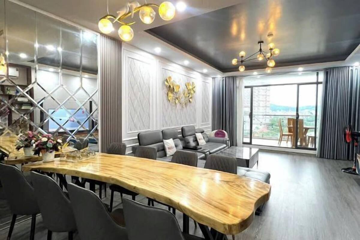 A modern dining area with a wooden table, grey chairs, a sofa, and a large window with a view.