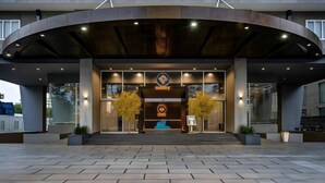 A modern building entrance with a curved roof, two symmetrical trees, and a blue seating area. - 3-bedroom Oasky Vung Tau with Partial Ocean View (Ho Chi Minh City)