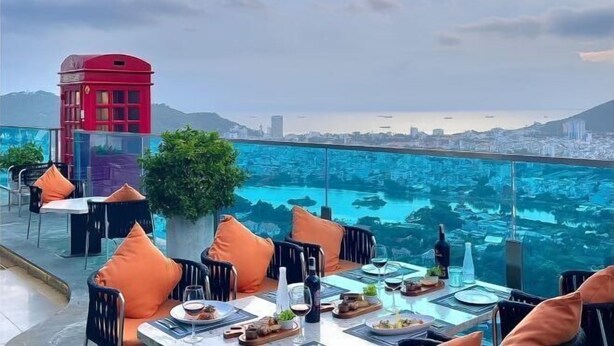 A rooftop dining area with tables and chairs, a red telephone booth, and a view of a cityscape and water. - 3-bedroom Oasky Vung Tau with Partial Ocean View (Ho Chi Minh City)