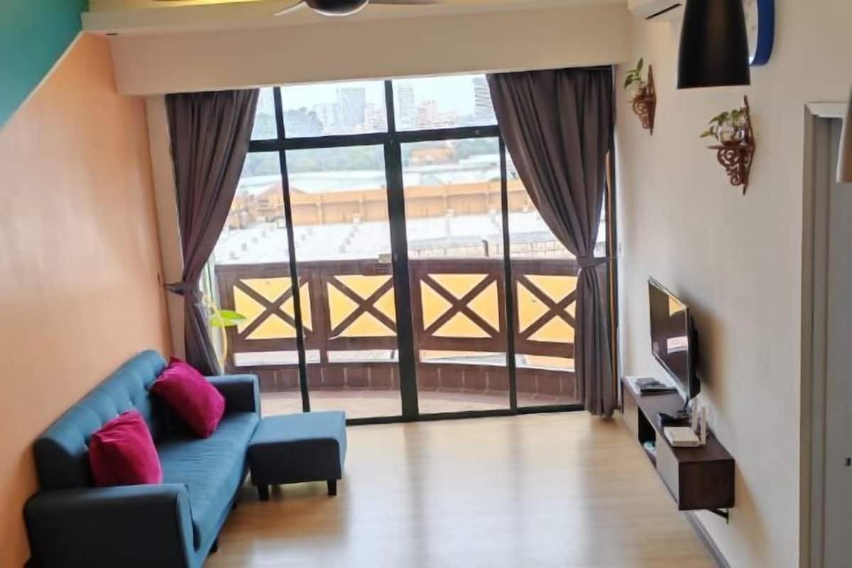 Un soggiorno con divano, televisione e balcone con vista sugli edifici.