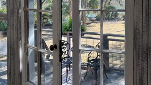 Una puerta de madera rústica con un panel de vidrio, que da a un patio al aire libre con sillas y mesas de metal.