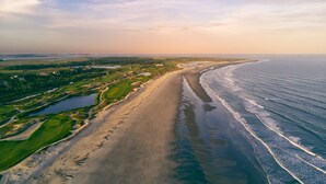 Vista aérea de una zona costera con una extensa playa de arena, un campo de golf y una masa de agua.