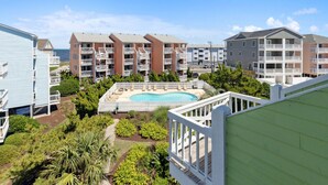 A residential building complex with multiple balconies, a swimming pool, and surrounding greenery.
