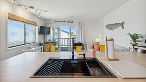 A modern kitchen with a stainless steel sink, a dining area with yellow chairs, and a large window providing a view of the outside.