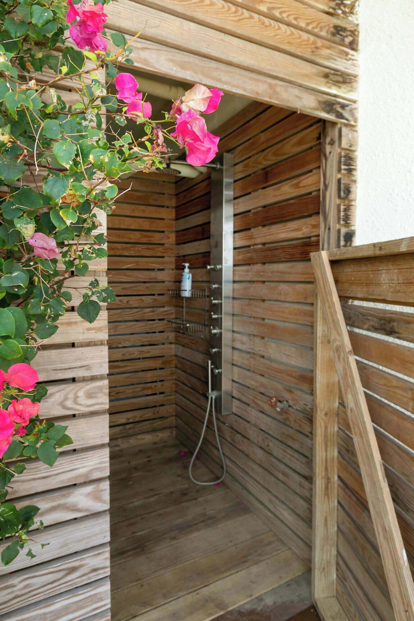 A wooden shower stall with a metal showerhead and a wooden door.
