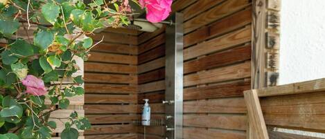 A wooden shower stall with a metal showerhead and a wooden door.