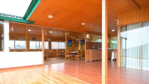 Una habitación amplia con pisos de madera y un techo alto, que incluye un comedor con sillas y una mesa, una zona de cocina con alacenas y un lavamanos, y ventanas grandes que dejan entrar luz natural.