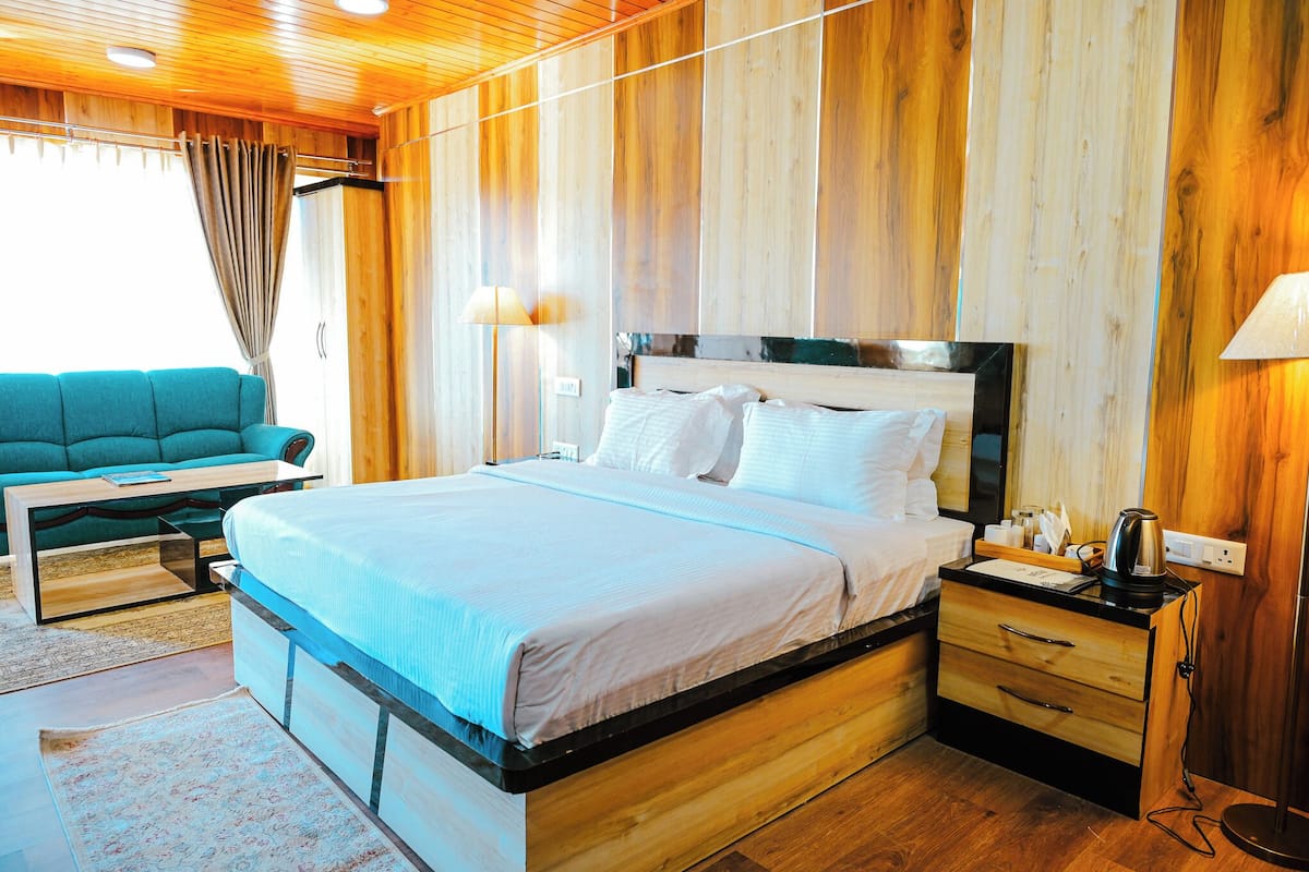 A wooden-paneled bedroom with a bed, bedside table, lamp, and a teal sofa.