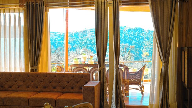 Una habitación con sofá, cama y balcón amueblado con ratán, con vistas a un paisaje montañoso.