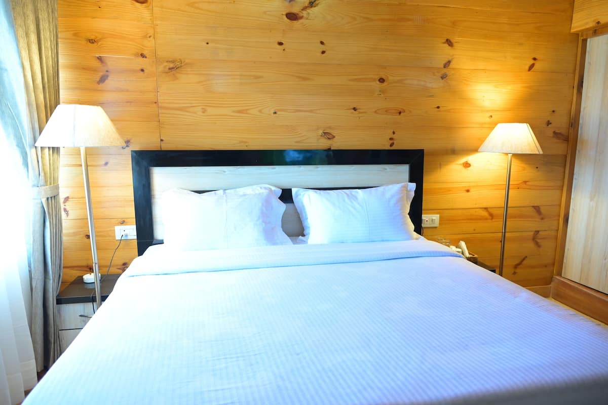 A neatly made bed with white linens in a room with wooden walls and two bedside lamps.