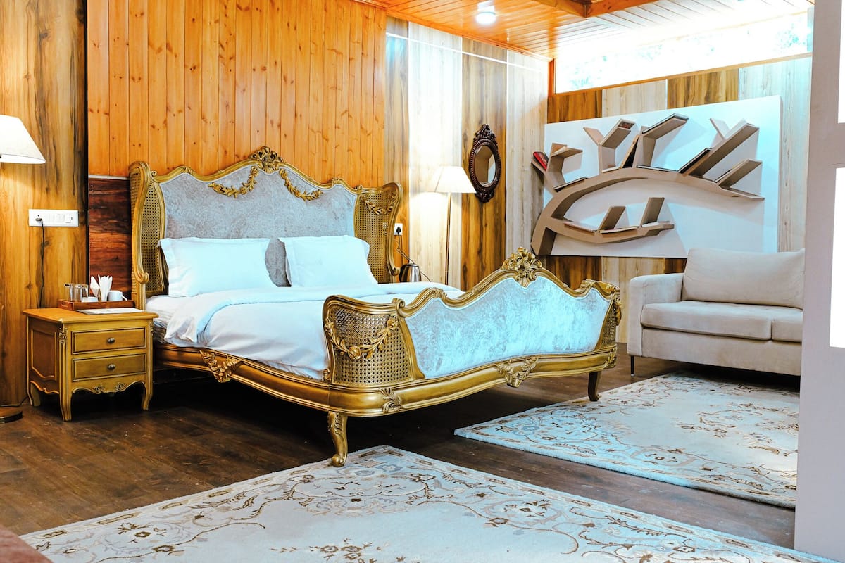 A bedroom with a large bed, a nightstand, a sofa, and a wall-mounted shelf with books.