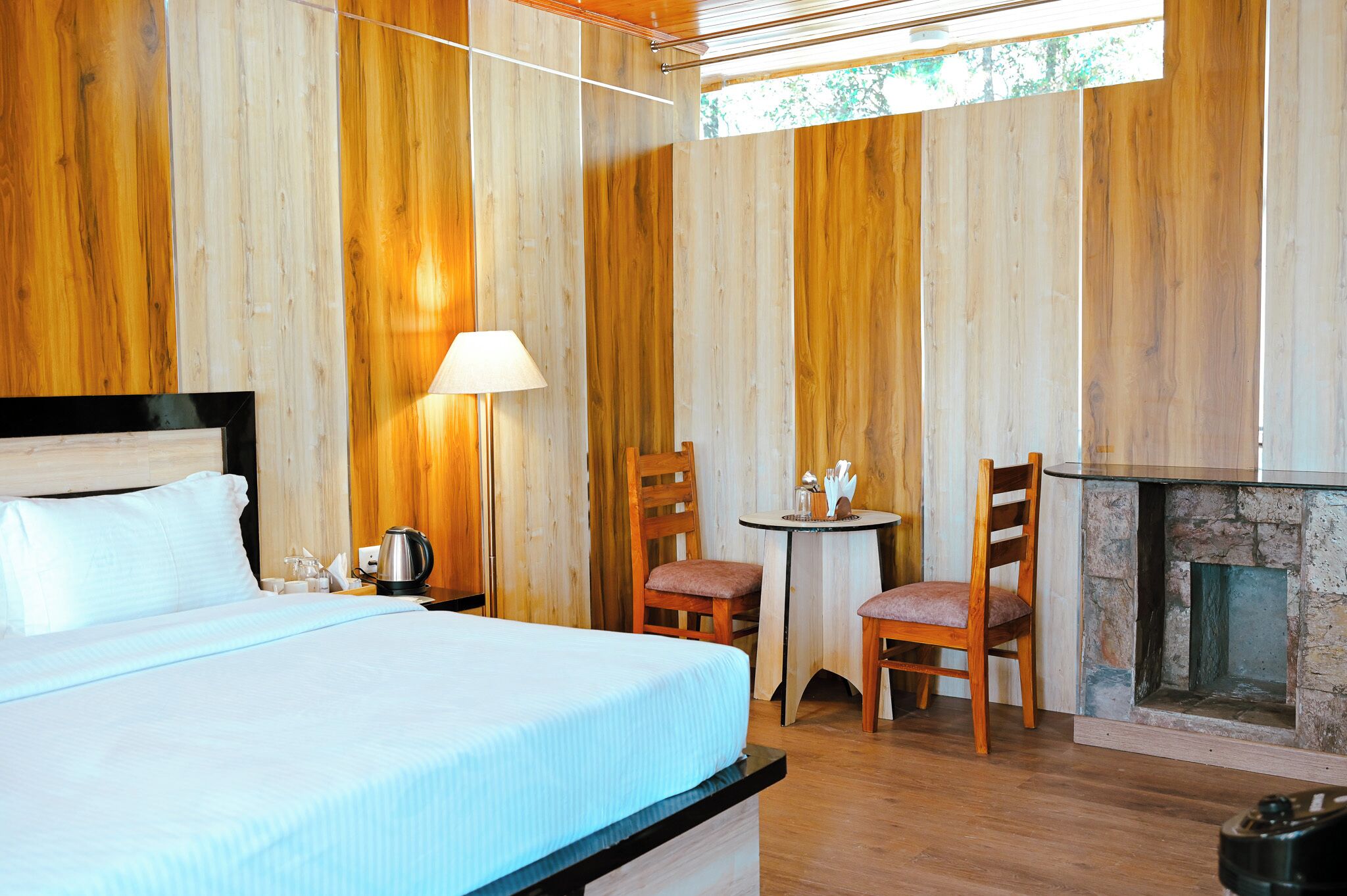 A hotel room with a bed, a table with chairs, a fireplace, and wooden walls.