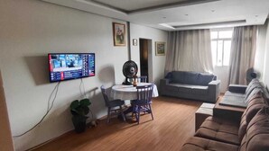 A living room with a television, a sofa, a dining table with chairs, and a fan. - Orchid farm and beach (Gonzaga Santos)