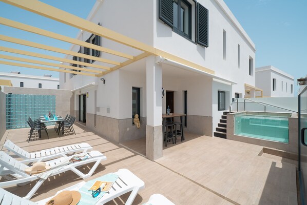Un espacio exterior techado con sillones de descanso, una piscina y una mesa de comedor.