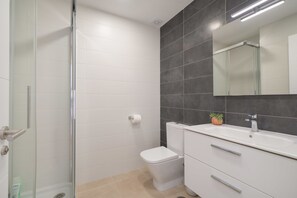 Un baño moderno con cabina de ducha de vidrio, inodoro blanco y tocador con espejo.