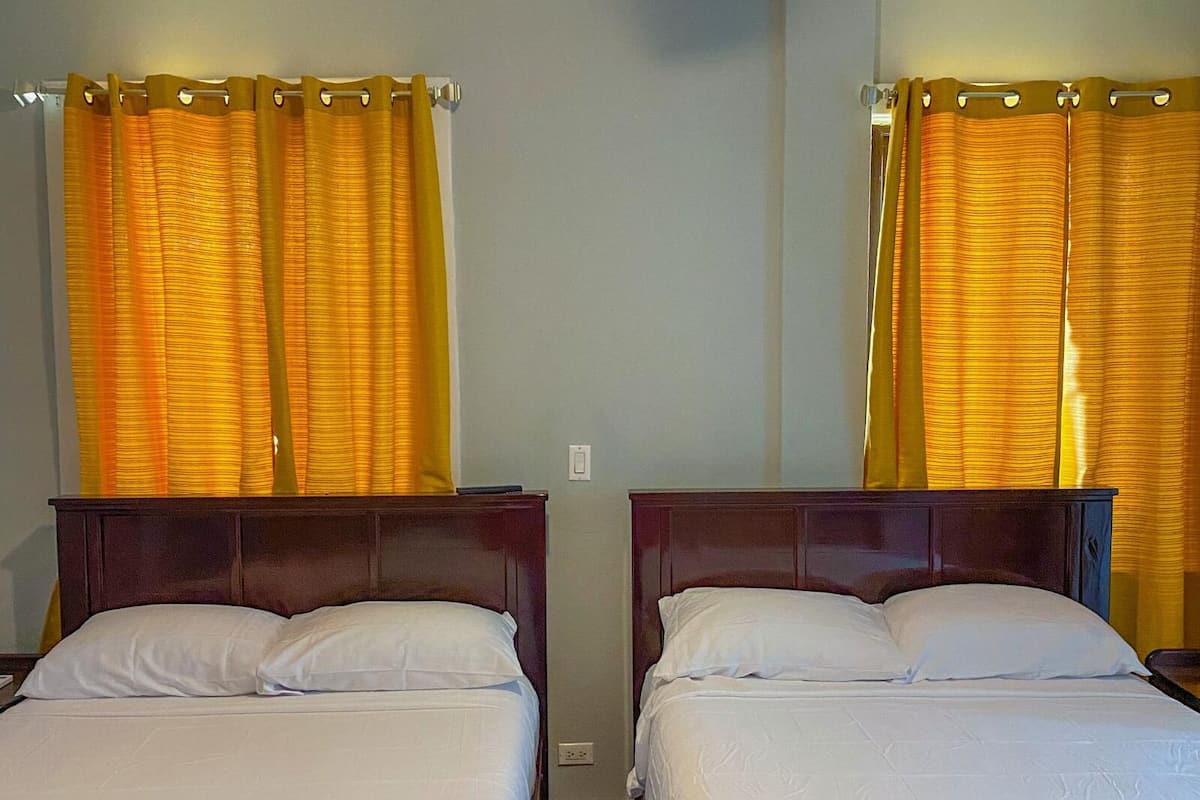Two single beds with wooden headboards in a room with yellow curtains.