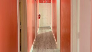 A corridor with pink walls, a white door at the end, and an exit sign above it. - Barana Hotel (Dangriga)