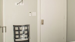 A hotel room with a bed, a chair, a television mounted on the wall, a door with a no smoking sign, and a ceiling fan. - Barana Hotel (Dangriga)