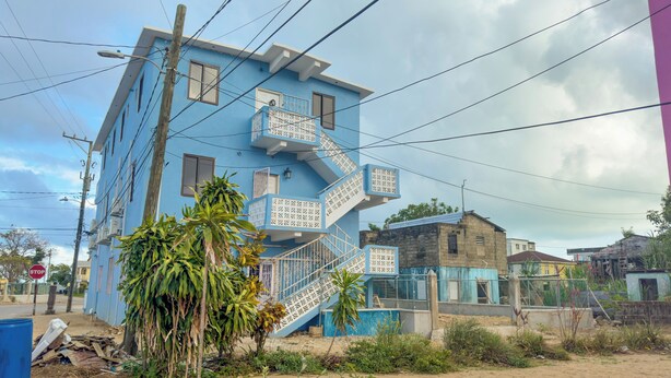 A multi-story building with a blue facade, a staircase with decorative railings, and a gated entrance. - Barana Hotel (Dangriga)