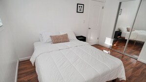A bedroom with a large bed, a bedside table, a mirror, and a door. - Beautiful & Centrally Located close to everything 3- bedroom home, AC, WiFi (Baldwin Park)