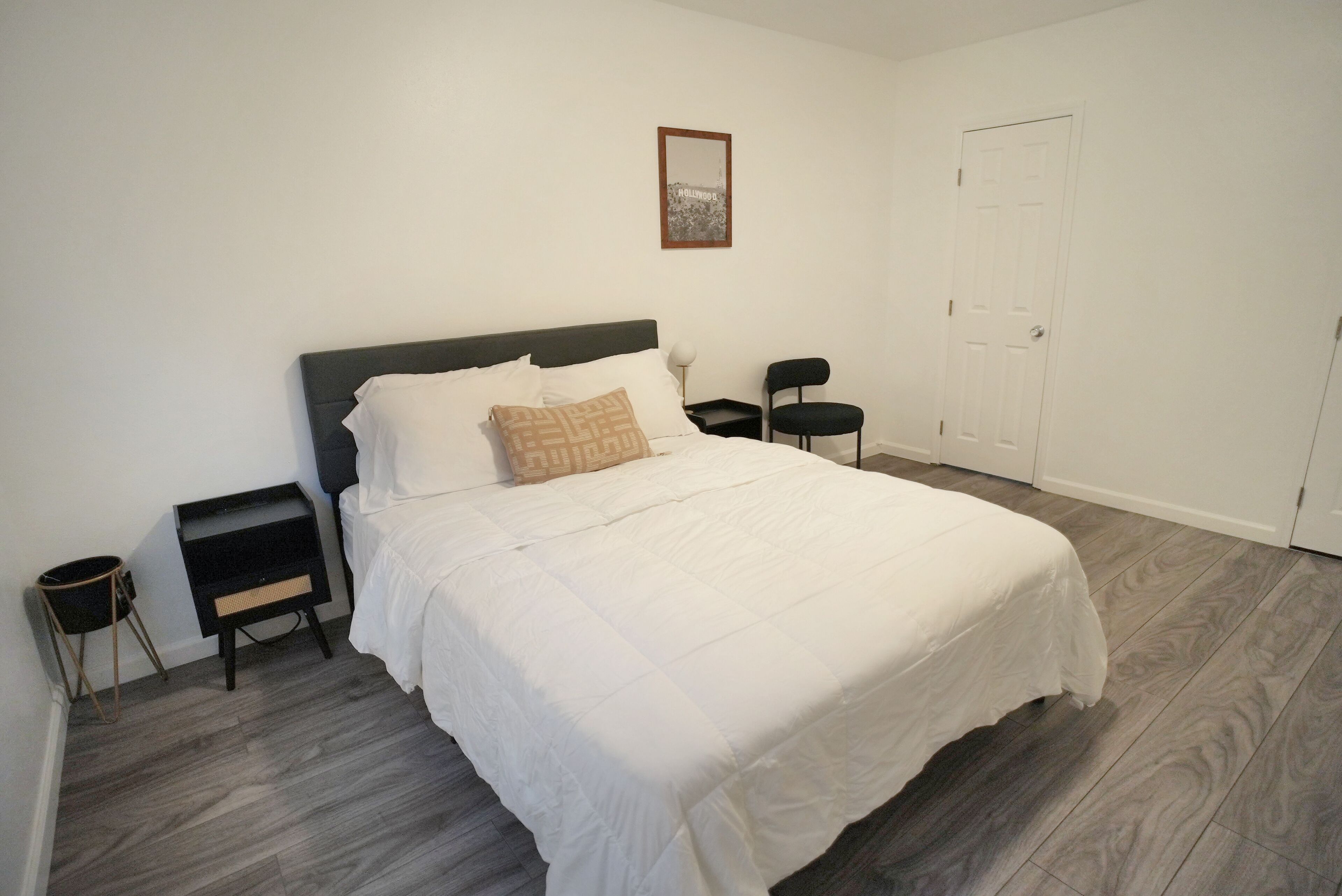A neatly arranged bedroom with a bed, a nightstand, a chair, and a door.