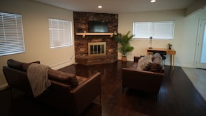 A living room with a stone fireplace, leather sofas, and a flat-screen TV. - Beautiful & Centrally Located close to everything 3- bedroom home, AC, WiFi (Baldwin Park)