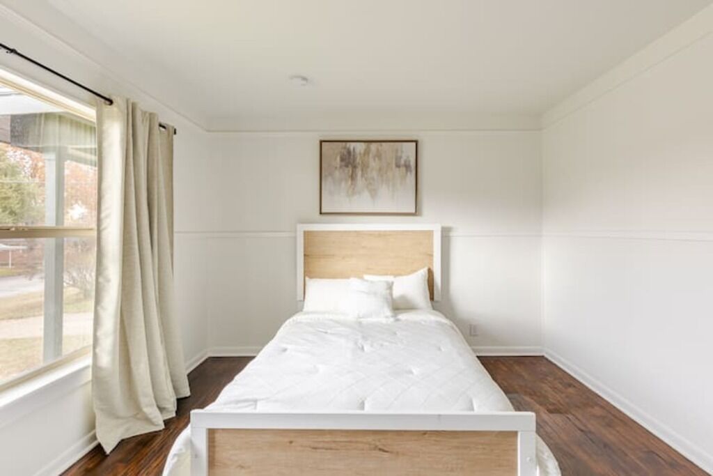 Une chambre à coucher avec un lit, une fenêtre avec des rideaux et un tableau accroché au mur.