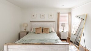Quarto com uma cama, duas mesas de cabeceira, um espelho e três quadros na parede.