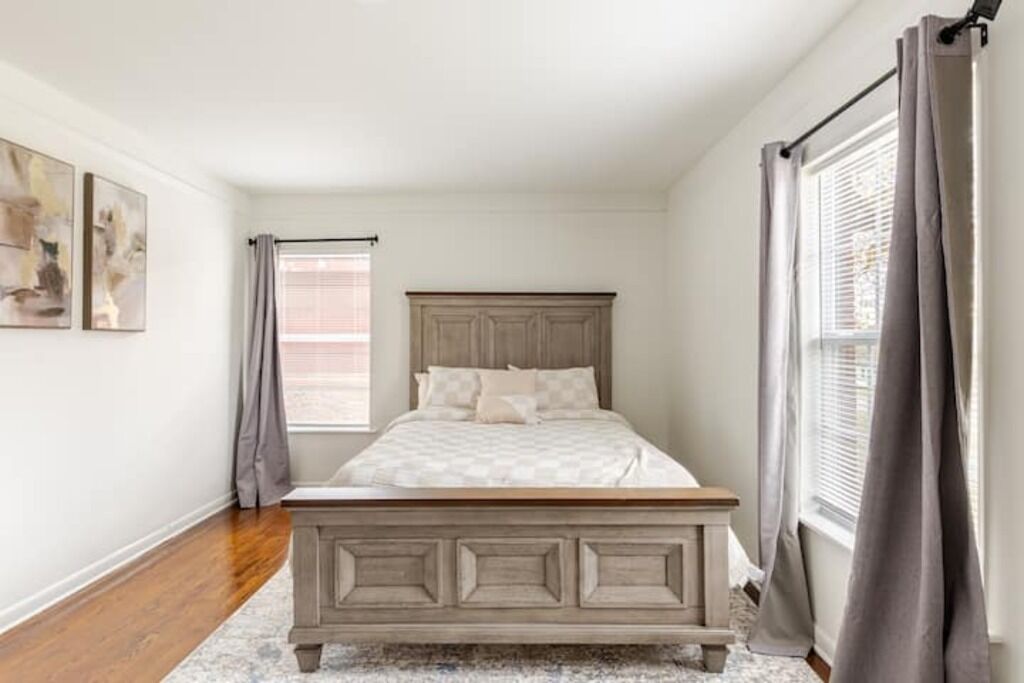A bedroom with a wooden bed, a window with curtains, and artwork on the wall.