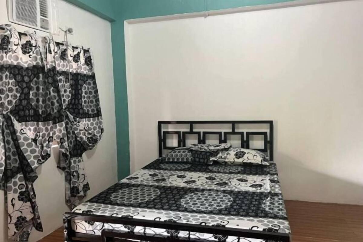 Une chambre à coucher avec un lit, une tête de lit et une fenêtre avec des rideaux.