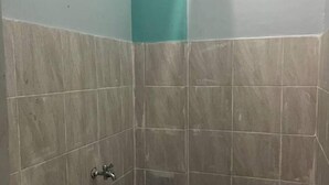A small, enclosed shower area with grey tiles and a blue bucket.