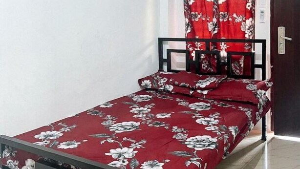 A small bed with a floral bedspread, a black metal frame, and a red curtain.