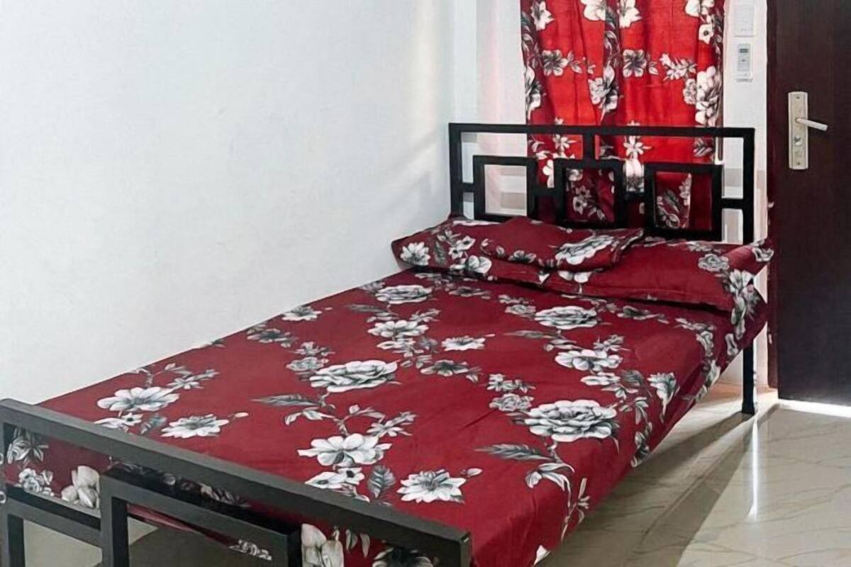 Un petit lit avec une couvre-lit à motifs floraux, un cadre en métal noir et un rideau rouge.