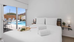Habitación de hotel moderna con una cama grande, vista a una piscina y una mesita con una lámpara.