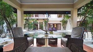 A glass-top dining table with wicker chairs in a courtyard with plants and a building in the background. - Luxurious Pattaya Pool Villa (Sattahip)