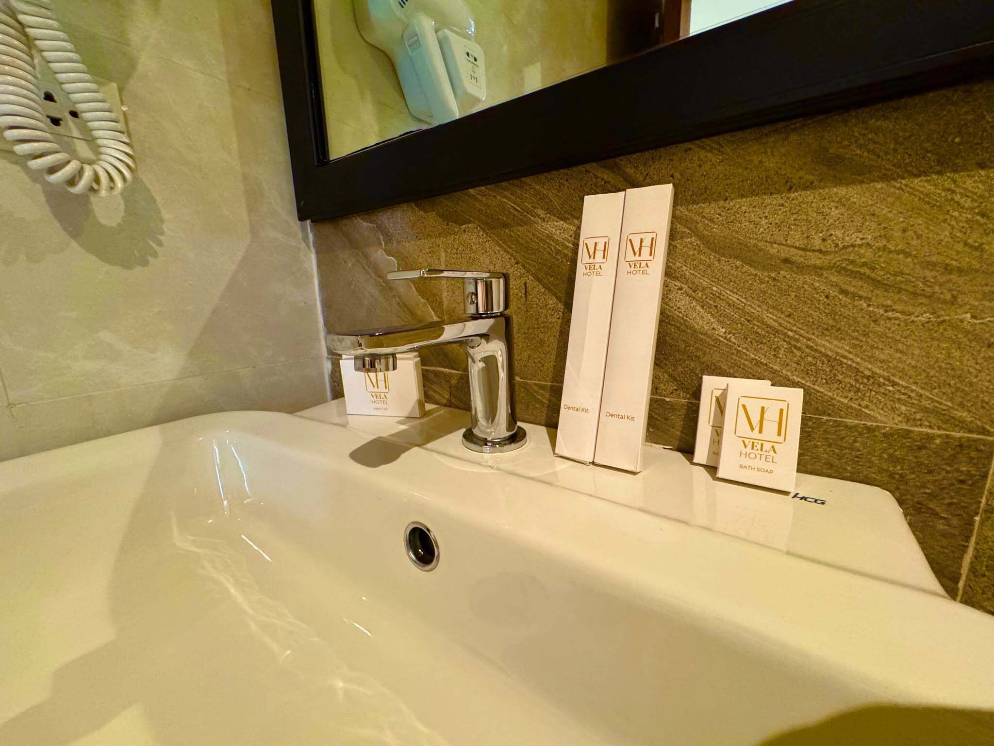 A hotel bathroom sink with a mirror above it, a telephone, and toiletries including a dental kit and bath soap.