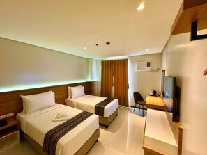 A hotel room with two beds, a desk, a chair, a TV, and an air conditioning unit. - VELA HOTEL (Legazpi)