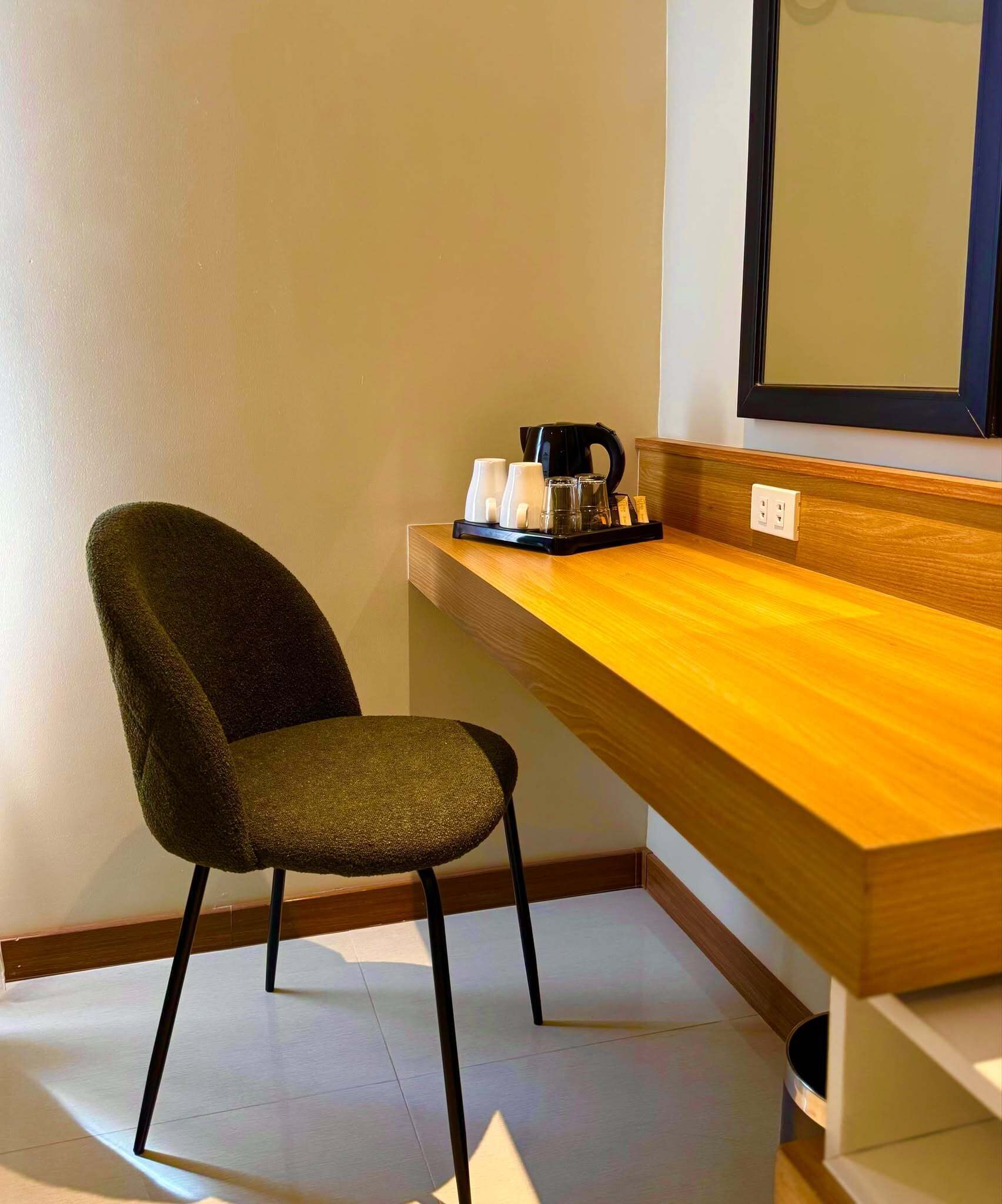 Une chambre moderne équipée d’un bureau en bois, d’une chaise, d’une machine à café et d’un miroir.