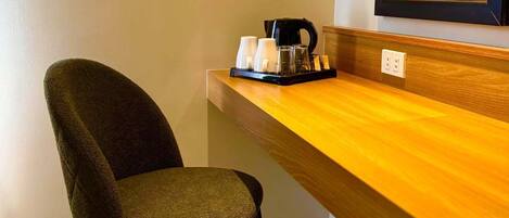 A modern room with a wooden desk, a chair, a coffee maker, and a mirror.