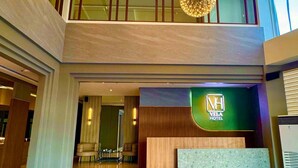 A modern hotel lobby with a reception desk, a high ceiling with spherical light fixtures, and a view to the upper floor.