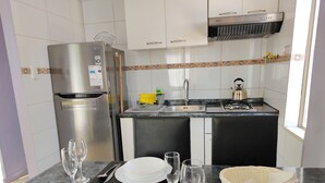 A compact kitchen with a refrigerator, stove, sink, and a dining area set with plates, glasses, and cutlery.
