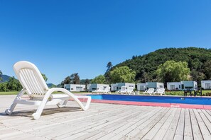 Een zwembadterras met witte ligbedden, een blauw zwembad en een beboste heuvel op de achtergrond.