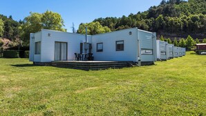 A row of mobile homes with a grassy field in the foreground and a forested hill in the background.