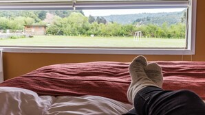 A bed with a view of a grassy field and trees through a window.