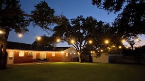 A backyard with a house, string lights, and a tree.