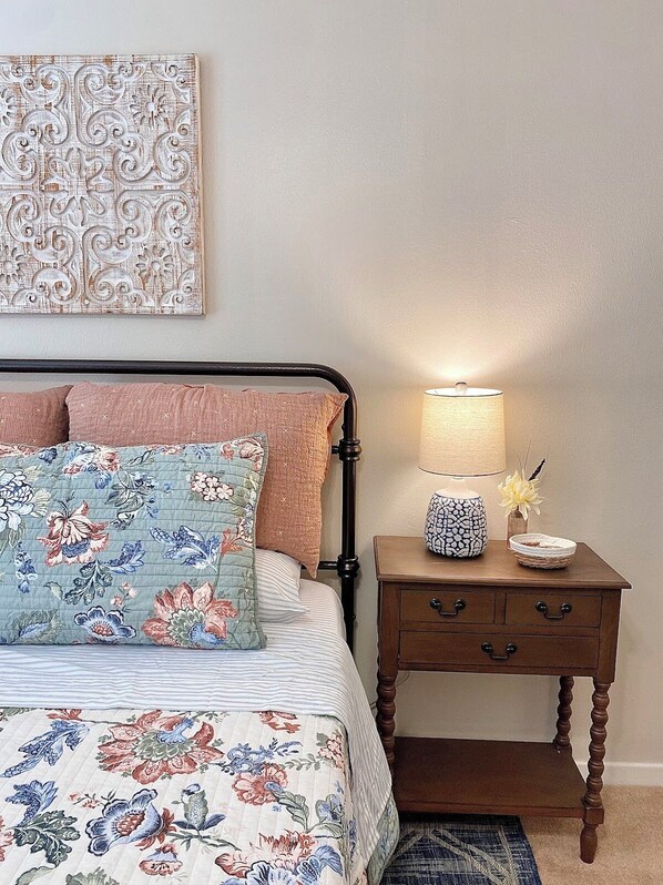 Un dormitorio con una cama, una mesita de noche con lámpara y un adorno en la pared.