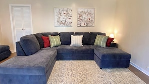 A sectional sofa with multiple cushions, a patterned rug, and two wall-mounted paintings.